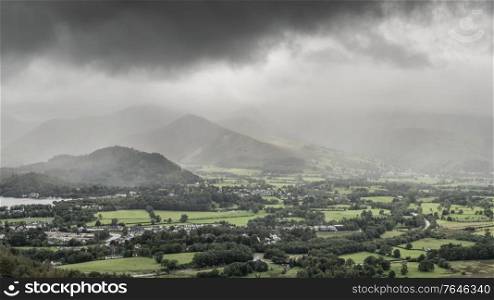 Beautiful landscape image across Derwentwater valley with falling rain drifting across the mountains onto the lush green countryside below