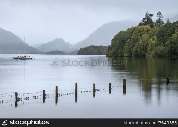 Beautiful landscape image of Derwentwater in English Lake District during late Summer morning with still water and misty mountains