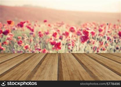 Beautiful landscape image of Summer poppy field under stuning sunset sky with cross processed retro effect with wooden planks floor