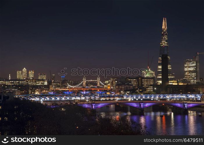 Beautiful landscape image of the London skyline at night looking. England, London, The Shard. The London skyline at night including The Shard with Tower Bridge and Canary Wharf.. Landscape image of the London skyline at night looking along the River Thames