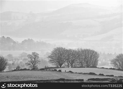 Beautiful landscape image of the Peak District in England on a hazy Winter day viewed from the lower slopes of Bamford Edge in black and white