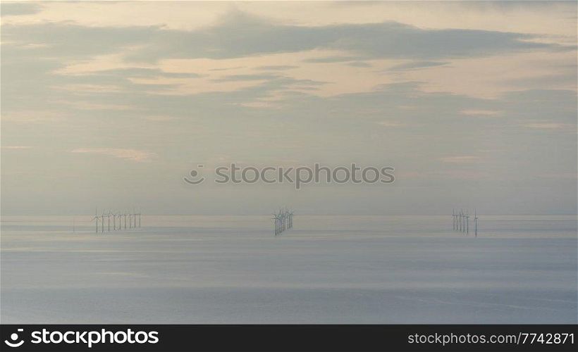 Beautiful landscape image of wind turbine farm off North coast of Wales with lovely pastel sunset colours
