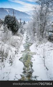Beautiful landscape of fast mountain stream at forest covered by snow