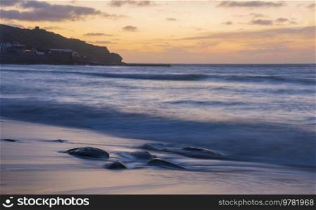 Beautiful landscape of Sennen Cove in Cornwall during sunset with moody sky and long exposure sea motion