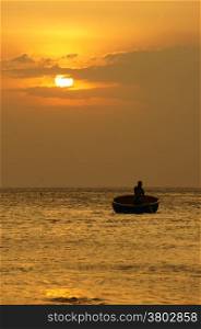 Beautiful landscape on ocean with silhouette of fisherman standing and rowing on circle boat at sunset, the sun go down, sky in brilliant yellow at sunset