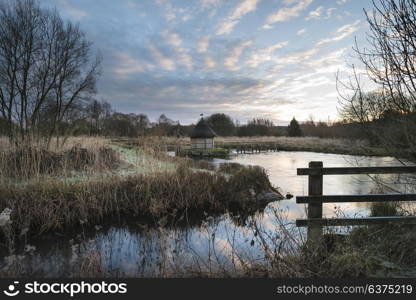 Beautiful landscape on Winter morning of eel traps over flowing river in English countryside