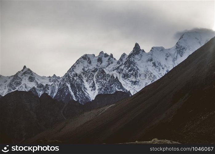 Beautiful landscape scenery of sunset at Passu in the dusk. Snow capped massif mountain peaks in Karakoram range with fog and clouds, Gojal Hunza. Gilgit Baltistan, Pakistan.