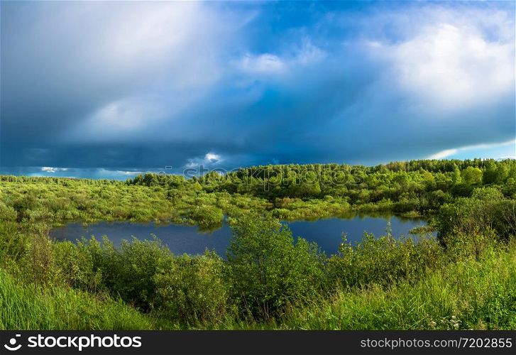 Beautiful landscape with a small lake, sunlit and disturbing storm sky.