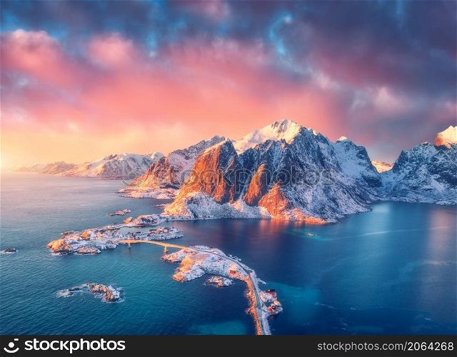 Beautiful landscape with blue sea, snowy mountains, rocks and islands, village, rorbu, road, bridge and pink sky at sunrise. Aerial view. Hamnoy in snow in winter in Lofoten islands, Norway. Top view