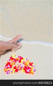 beautiful legs and Hawaiian floral lei near the sea on white gentle sand