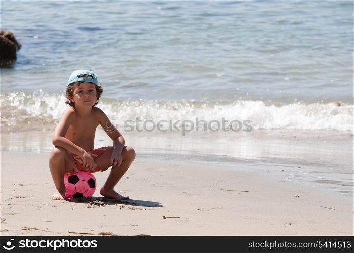 Beautiful little boy on the beach with a soccer ball