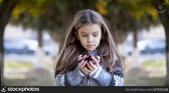 Beautiful little girl holding a chestnut in autumn park