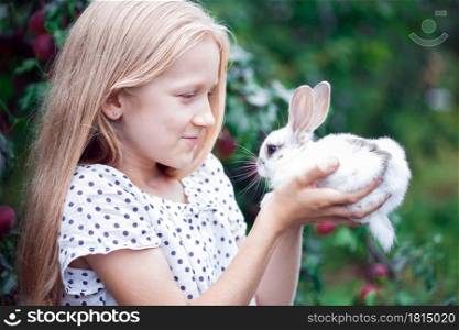 beautiful little girl holding in hands white rabbit at the garden