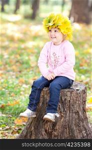 beautiful little girl in a wreath of maple leaves sitting on stump