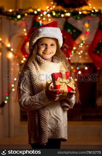 Beautiful little girl in red hat holding sparkling gift box