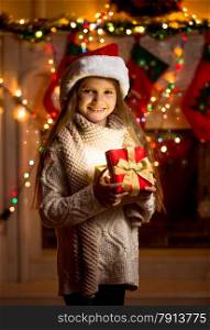 Beautiful little girl in red hat holding sparkling gift box