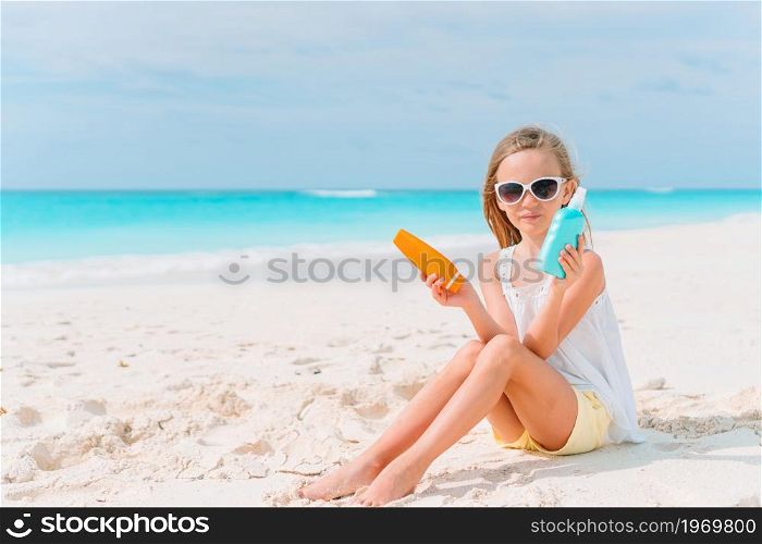 Beautiful little girl on the beach with sun cream bottle. Sun protection. Cute little girl at beach during summer vacation