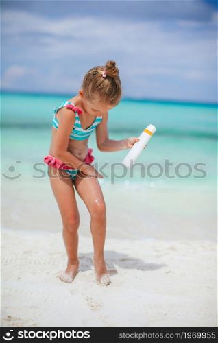 Beautiful little girl on the beach with sun cream bottle. Sun protection. Cute little girl at beach during summer vacation