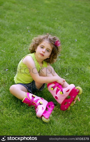 Beautiful little girl sit on the park grass with roller skates