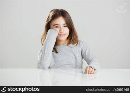 Beautiful little girl sitting behind a desk and smiling, against a gray background