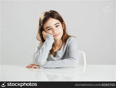 Beautiful little girl sitting behind a desk with a distracted expression, against a gray background
