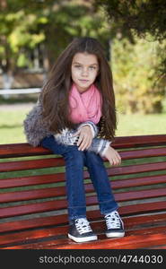 Beautiful little girl sitting on a bench in autumn park