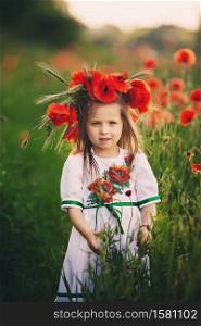 beautiful little girl with a wreath of poppies in a white dress and a bouquet of wildflowers. cute child in poppy field.. beautiful little girl with a wreath of poppies in a white dress and collects a bouquet of wildflowers. cute child in poppy field