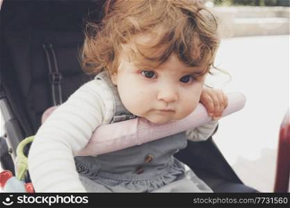 Beautiful little girl with curly hair sitting in her stroller