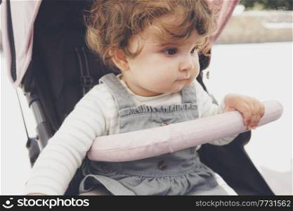 Beautiful little girl with curly hair sitting in her stroller