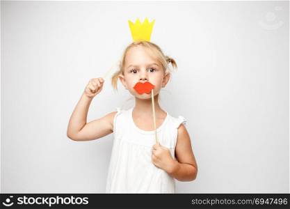 Beautiful little girl with paper crown and red lips posing on white background at home.. Beautiful little girl with paper crown and red lips posing on white background at home