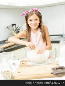 Beautiful little girl with pink bow on hair making dough in big bowl
