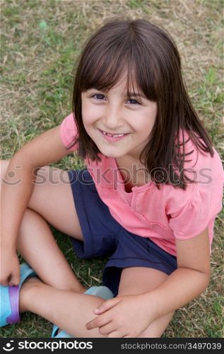 Beautiful little girl with pink shirt sitting on the grass