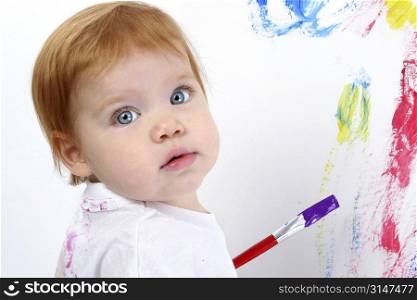 Beautiful little redhead baby painting at poster board. Bright blue eyes and red hair.