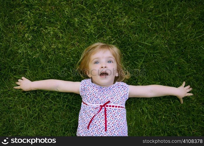 Beautiful little toddler girl happy lying on the green grass