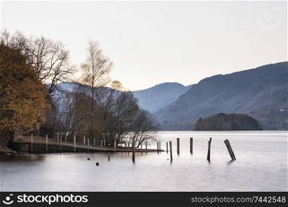 Beautiful long exposure landscape image of Derwent Water in Lake District during Autumn Fall sunrise with soft pastel colors