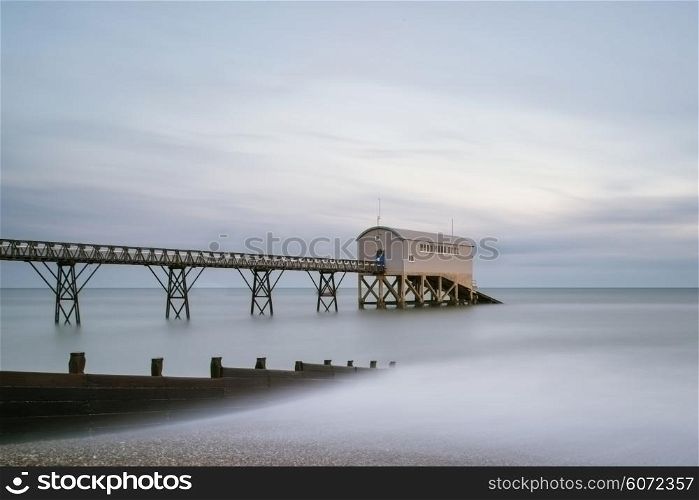 Beautiful long exposure landscape image of lifeboat jetty at sea