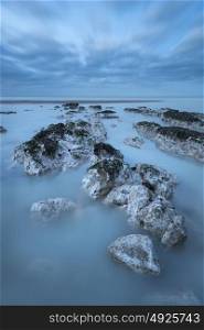 Beautiful long exposure landscape image of low tide beach with rocks at sunrise