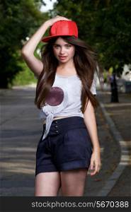 beautiful long haired teen model on pave. red cap, grey t-shirt, dark blue shorts