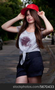 beautiful long haired teen model on road. red cap, grey t-shirt, dark blue shorts