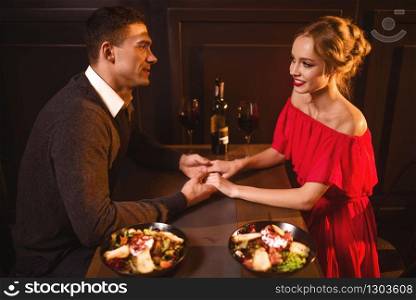 Beautiful love couple in restaurant, romantic evening. Elegant woman in red dress and her man sitting at the table, anniversary celebration. Love couple in restaurant, romantic evening