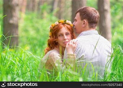 Beautiful lovers sitting on grass in forest, resting outdoors, gentle romantic feelings, happy wedding day, young new family