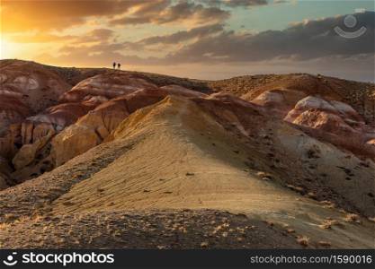 Beautiful low angle shot of two tiny human figures walking towards sunset on top of massive red mountain in Kyzyl-Chin valley, also called Mars valley. Golden hour. Altai, Siberia, Russia.. Beautiful low angle shot of two tiny human figures walking towards sunset on top of massive red mountain in Kyzyl-Chin valley, also called Mars valley. Golden hour. Altai, Siberia, Russia