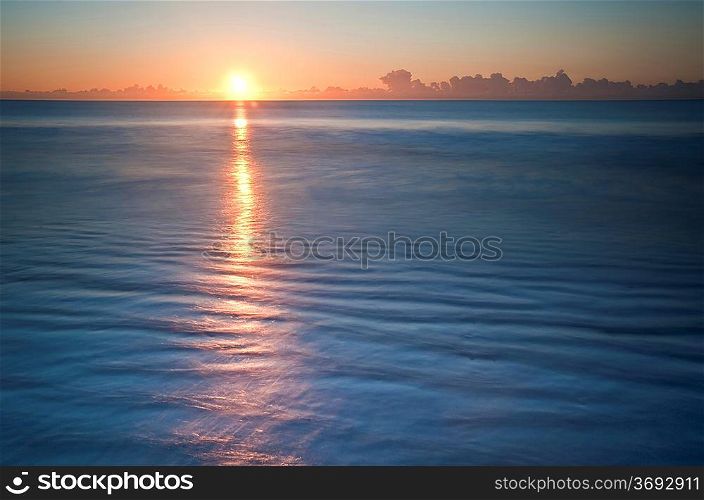 Beautiful low point of view along beach at low tide out to sea with vibrant sunrise sky