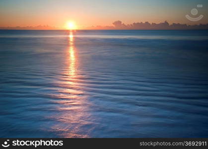 Beautiful low point of view along beach at low tide out to sea with vibrant sunrise sky