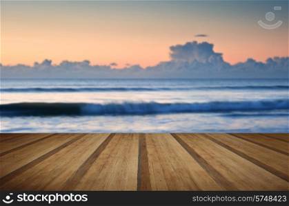 Beautiful low point of view along beach at low tide out to sea with vibrant sunrise sky with wooden planks floor