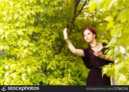 Beautiful makeup girl wearing black tunic and an antique jewels, green leaves on background
