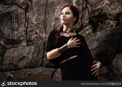 Beautiful makeup girl wearing black tunic and an antique jewels, rocky wall on background