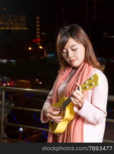 Beautiful Malay female with ukelele; city lights in background