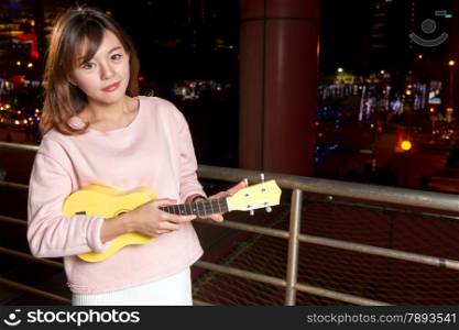 Beautiful Malay female with ukelele; city lights in background