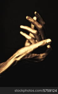 beautiful man&rsquo;s hands in golden paint on black background close up